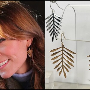 May include: A pair of gold leaf-shaped earrings on a display stand. The earrings are made of metal and have a delicate, intricate design.