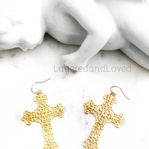 May include: A pair of gold filigree cross earrings. The earrings are delicate and intricate, with a floral design. They are perfect for adding a touch of elegance to any outfit.