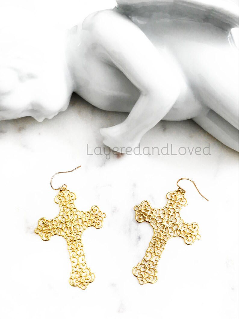 May include: A pair of gold filigree cross earrings. The earrings are delicate and intricate, with a floral design. They are perfect for adding a touch of elegance to any outfit.