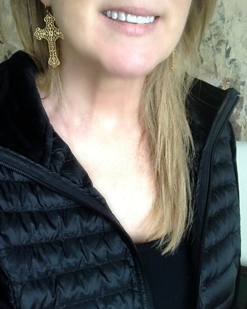 May include: A woman wearing a black puffer jacket with a zipper closure. She is wearing gold cross earrings.