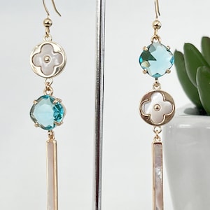 May include: Gold tone earrings with blue and white stones. The earrings feature a flower-shaped pendant with a white stone and a blue stone.