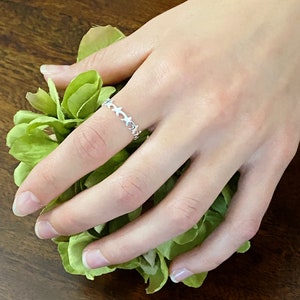 Puede incluir: Un anillo de plata con una cadena delicada de eslabones en forma de estrella. El anillo se lleva en el dedo índice de una mano.