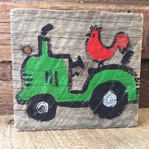 May include: A green toy tractor with a red rooster riding on the back. The tractor is painted on a piece of weathered wood.