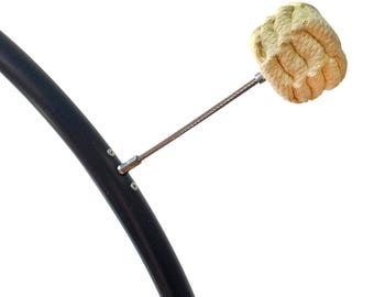 May include: A black curved hoop featuring a single metal wire spoke that extends outward, terminating in a textured, light beige, spherical wick head made of tightly wound material, designed for fire performance equipment.