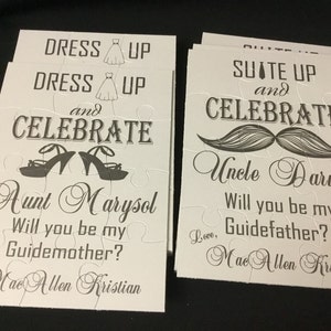 May include: Two white puzzle pieces with black text and illustrations. The first piece says "Dress Up and Celebrate" with a pair of high heels and the text "Aunt Marysol Will you be my Guidemother? Love, Mae Allen Kristian". The second piece says "Suit Up and Celebrate" with a mustache and the text "Uncle Darwin Will you be my Guidefather? Love, Mae Allen Kristian".