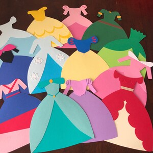 May include: A collection of 11 paper princess dress cutouts in various colors, including pink, blue, yellow, green, and red. The dresses are all different styles and have intricate details.