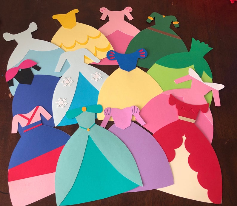 May include: A collection of 11 paper princess dress cutouts in various colors, including pink, blue, yellow, green, and red. The dresses are all different styles and have intricate details.