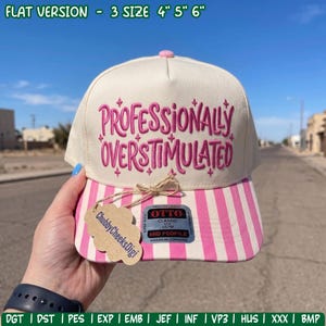May include: A cream-colored baseball cap with a pink striped brim and the embroidered pink text "PROFESSIONALLY OVERSTIMULATED" on the front. The cap features a sticker on the brim and a tan tag labeled "ChubbyCheeksDigi" tied with twine.