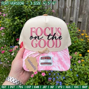 May include: A cream-colored baseball cap with a pink tie-dye brim featuring the embroidered text "FOCUS on the GOOD" in pink and black. The cap includes a tag labeled "ChubbyCheeksDigi" and an Otto brand sticker, with text indicating 4", 5", 6" sizes.