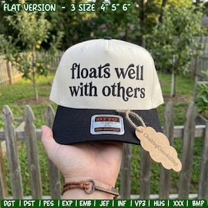 Puede incluir: Una gorra de béisbol color crema con visera negra que presenta el texto negro bordado 'floats well with others' en la parte frontal. Una pegatina rectangular en la visera dice 'OTTO' y una etiqueta de papel marrón está atada con un cordel.
