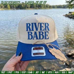 May include: A cream-colored baseball cap with a blue brim and the embroidered blue text RIVER BABE on the front. The cap features a sticker on the brim labeled OTTO CLASSIC FIT MID PROFILE and a brown tag attached with twine reading ChubbyCheeksDigi.