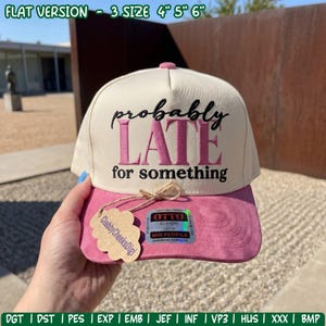 May include: A cream-colored baseball cap with a pink brim featuring the embroidered text 'probably LATE for something' in black and pink. A cloud-shaped tag is attached to the brim, and a holographic sticker is visible on the front panel.