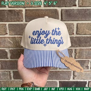 May include: A cream-colored baseball cap with a blue striped brim. The front features blue embroidered text that reads enjoy the little things with small star accents. A brown cardboard tag attached to the brim displays the text ChubbyCheeksDigi.