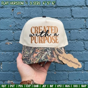 May include: A cream-colored baseball cap with a camouflage-patterned brim. The front features the embroidered text "CREATED with a PURPOSE" in brown and black. A brown, cloud-shaped tag attached to the brim reads "ChubbyCheeksDigi".