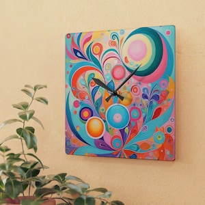 May include: Square wall clock with a colorful abstract floral design. The clock face features a vibrant mix of blues, pinks, oranges, and greens. Black clock hands indicate the time. The clock is mounted on a light beige wall.