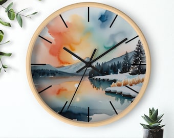May include: Round wall clock with a watercolor landscape design. The clock face features a mountain scene with a lake, trees, and a colorful sky in shades of orange, blue, and yellow. The clock has black hands and a light wood frame.