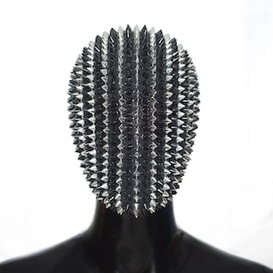 May include: A black head covering featuring a dense, uniform pattern of sharp, metallic silver-colored spikes arranged in vertical rows. The spikes are conical and reflective, covering the entire surface of the rounded, form-fitting headpiece.