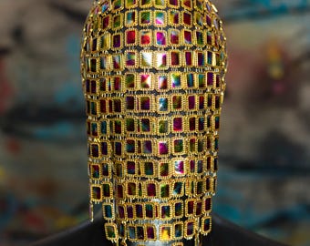 Könnte beinhalten: Eine goldene Kettenhemdmaske mit regenbogenfarbenen quadratischen Verzierungen. Die Maske befindet sich auf einem schwarzen Hintergrund. MASK BY CRYPTIC NINE © www.crypticnine.com