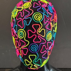 Könnte beinhalten: Eine schwarze Maske mit einem bunten Design aus Wirbeln und abstrakten Formen. Die Maske besteht aus Netzstoff und hat ein neonpinkes, grünes, blaues, gelbes und violettes Design.