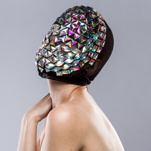 May include: A person wearing a black mesh mask with iridescent triangular sequins covering the face.
