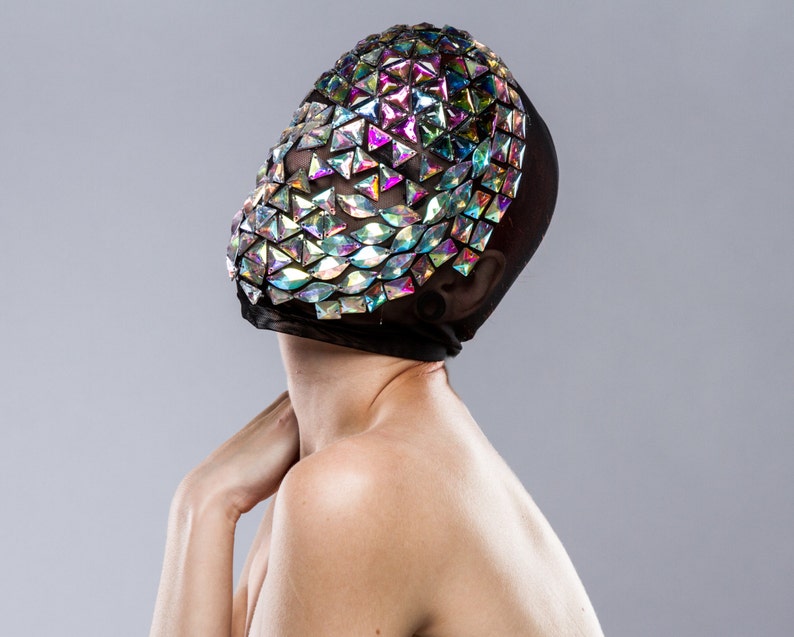 May include: A person wearing a black mesh mask with iridescent triangular sequins covering the face.