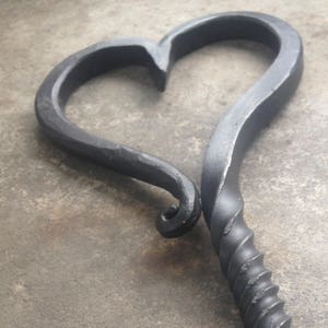 Pode incluir: Um ati&ccedil;ador de fogo de metal preto em forma de cora&ccedil;&atilde;o com uma al&ccedil;a torcida.