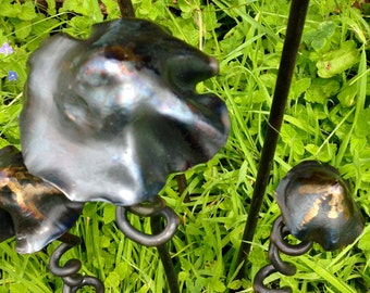 Könnte beinhalten: Ein Set aus fünf Metall-Gartenskulpturen in Form von Pilzen. Die Skulpturen sind aus dunklem Metall mit einer strukturierten Oberfläche und haben einen rustikalen Look. Sie sind in einer Gruppe auf einem Bett aus grünem Gras angeordnet.