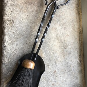Pode incluir: Um conjunto de duas ferramentas de lareira de metal preto com al&ccedil;as em forma de cora&ccedil;&atilde;o e uma p&aacute; de p&oacute; de metal preto correspondente com uma al&ccedil;a de madeira e uma escova preta.