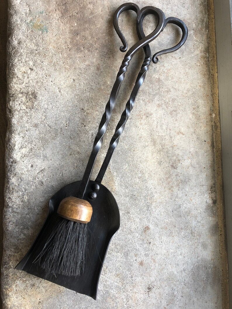 Pode incluir: Um conjunto de duas ferramentas de lareira de metal preto com al&ccedil;as em forma de cora&ccedil;&atilde;o e uma p&aacute; de p&oacute; de metal preto correspondente com uma al&ccedil;a de madeira e uma escova preta.