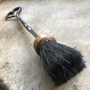 Pode incluir: Uma escova de lareira preta com uma al&ccedil;a de metal torcida e uma base de madeira. A al&ccedil;a tem a forma de um cora&ccedil;&atilde;o.