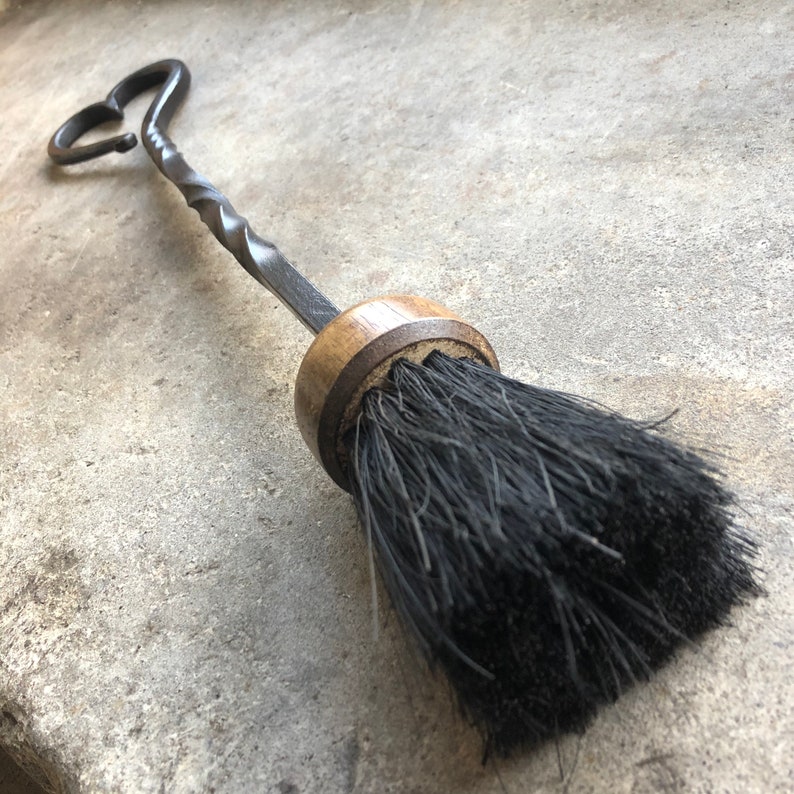 Pode incluir: Uma escova de lareira preta com uma al&ccedil;a de metal torcida e uma base de madeira. A al&ccedil;a tem a forma de um cora&ccedil;&atilde;o.
