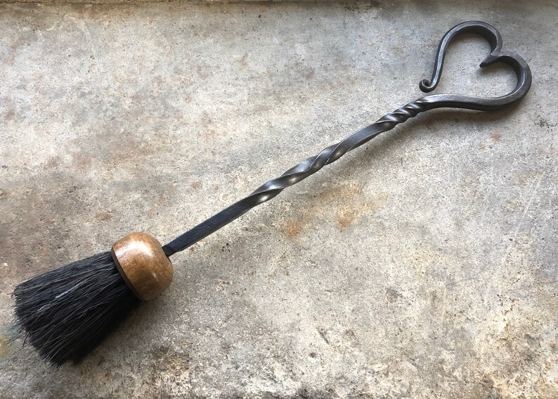 Pode incluir: Uma escova de lareira de metal preto com uma al&ccedil;a torcida e uma parte superior em forma de cora&ccedil;&atilde;o. A escova tem uma al&ccedil;a de madeira e cerdas pretas.