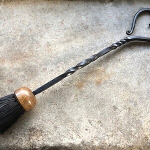 Pode incluir: Uma escova de lareira preta com uma pega de madeira e uma pega de metal em forma de cora&ccedil;&atilde;o.
