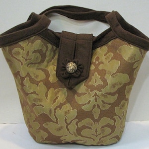 May include: A brown and gold patterned tote bag with a brown fabric handle and a decorative button.