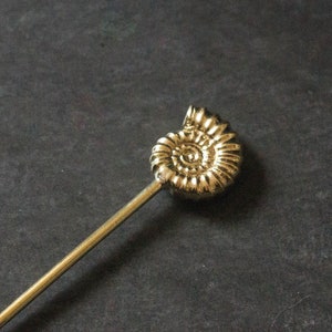 May include: A gold-coloured metal cocktail stick with a spiral ammonite design at the top.