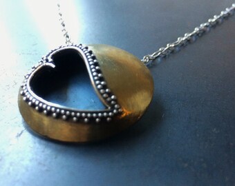 May include: A gold pendant necklace with a heart-shaped cutout surrounded by silver beads. The pendant is attached to a silver chain.
