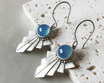 May include: A pair of silver earrings with a blue chalcedony stone set in a geometric design. The earrings have a delicate, modern look.