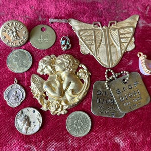 May include: A collection of vintage metal charms and coins, including a Detroit Police badge, a butterfly-shaped pendant, and two dog tags. Other items include a coin with a woman's profile and a small pendant with a religious figure.