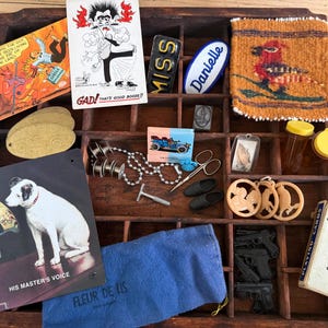 May include: A wooden printer's tray filled with various vintage items. Includes a metal sign with a dog and gramophone, playing cards, a blue pouch, and several small trinkets. The tray contains a variety of colors and textures.