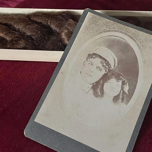 May include: A black and white photograph of a young couple. The man is wearing a sailor hat and the woman is wearing a dress. The photo is in an oval frame.