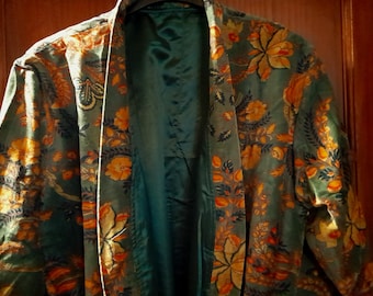 May include: A teal kimono-style jacket featuring a vibrant floral pattern in shades of orange, yellow, and dark green. The garment has long sleeves, a wide collar, and a solid dark teal interior lining, providing a structured open-front silhouette.