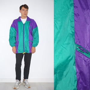 Peut inclure: Une veste coupe-vent bicolore turquoise et violette avec une fermeture éclair. La veste a un col montant et deux poches sur le devant.