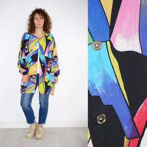 Könnte beinhalten: Ein langärmliges, übergroßes Hemd mit einem farbenfrohen abstrakten Druck mit geometrischen Formen und leuchtenden Farben wie Blau, Pink, Gelb und Rot. Das Hemd hat einen Knopfleisten vorne.
