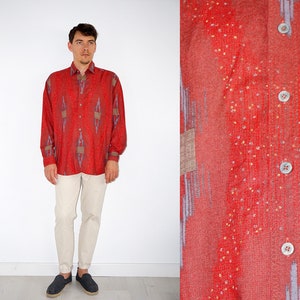 May include: A red long-sleeved button-down shirt with a geometric pattern in shades of blue and brown. The shirt has a relaxed fit and a collar.