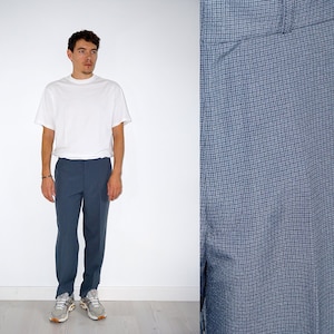 May include: A person wearing a white t-shirt and blue checkered pants. The pants have a subtle pattern and a straight leg fit.