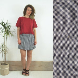 Pode incluir: Uma blusa vermelha de manga curta com uma borda de renda branca e uma saia xadrez branca e preta.