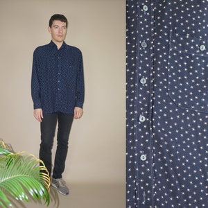 Op de afbeelding: Een donkerblauw, lang mouwig overhemd met knopen en een wit patroon van kleine, abstracte vormen. Het overhemd heeft een borstzak en een knoopsluiting aan de voorkant.