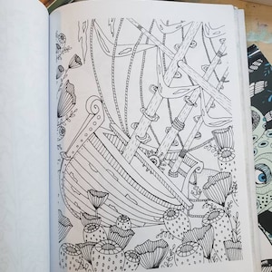 A coloring book opened to a shipwreck at the bottom of the ocean drawing in black and white
