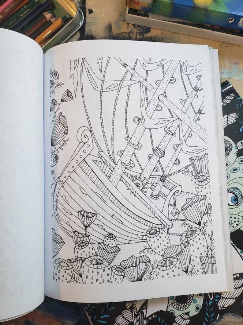 A coloring book opened to a shipwreck at the bottom of the ocean drawing in black and white