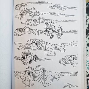 Black and white coloring book page of an illustration of a puffer fish and lion fish swimming along with a school of stingrays